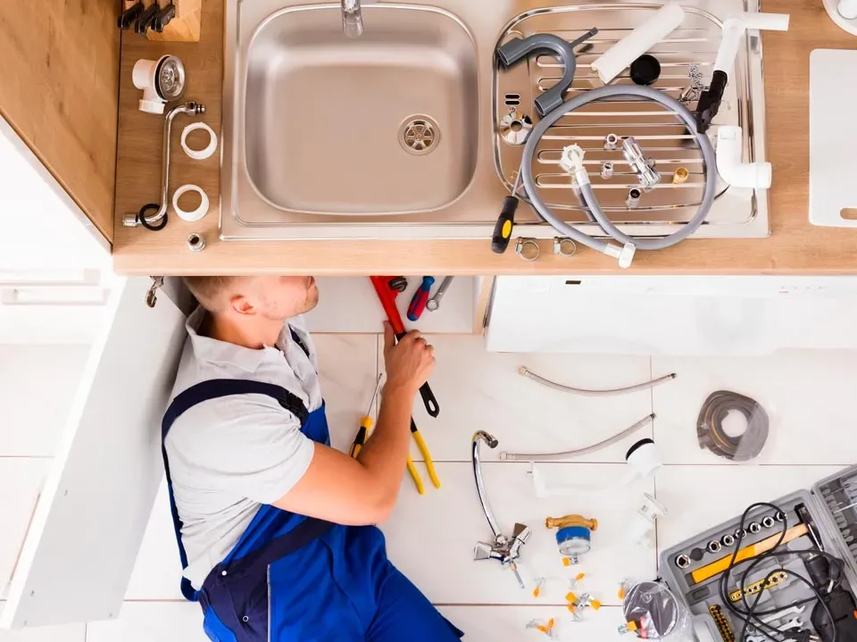 Plumber fitting pipework beneath a kitchen sink